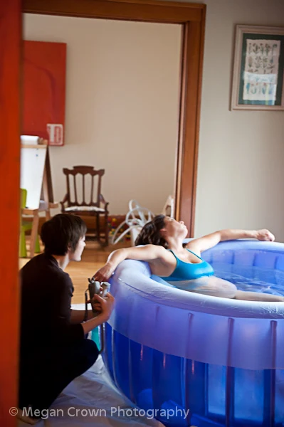 The Safety of Waterbirth A pregnant person in a birthing pool leans back with eyes closed while another offers support beside them, reflecting the calm and reassurance of a Bloomington home birth in a comfortable home setting.