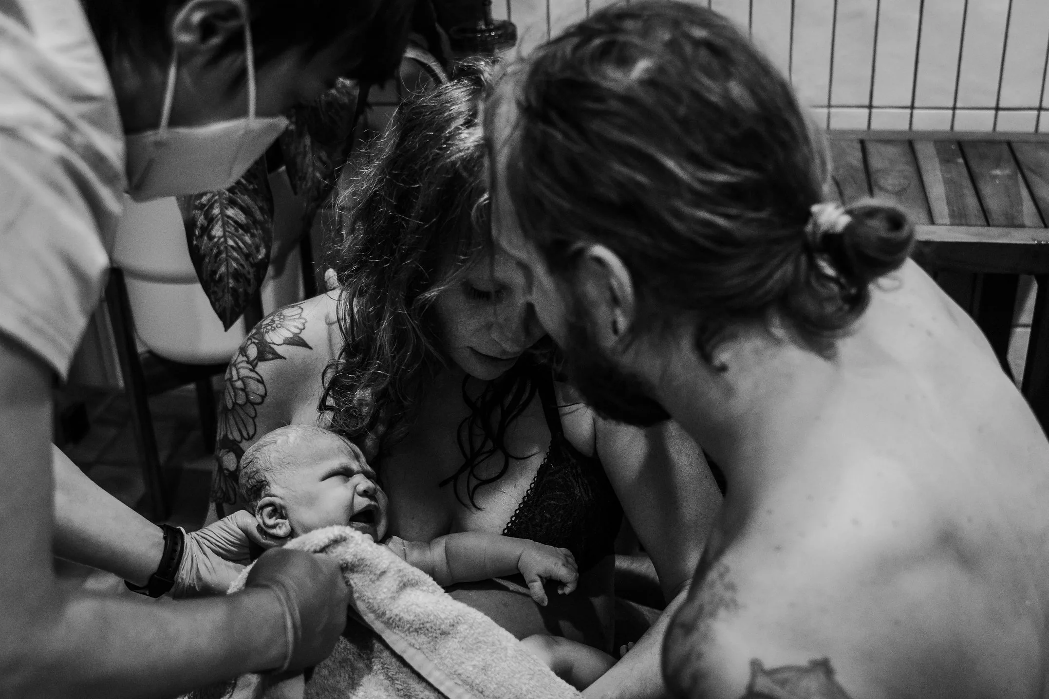 A woman holds a newborn baby while a man and a healthcare worker assist, all in a cozy home birth setting supported by St. Paul midwives.