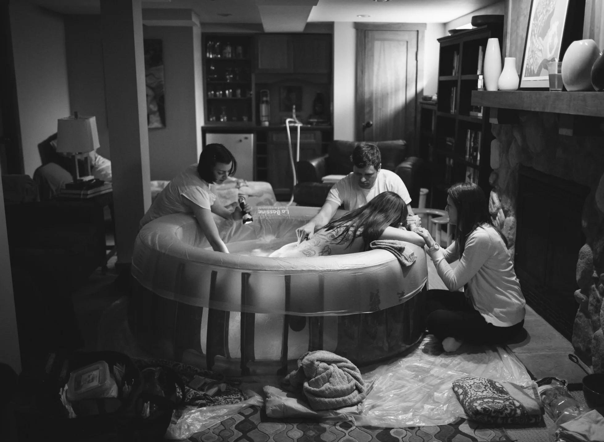 Four people are gathered around an inflatable birthing pool in a living room, with one person inside the pool and others offering support during a Brooklyn Park waterbirth.